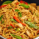 Closeup of a steaming plate of chicken lo mein noodles mixed with chicken pieces.